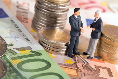 Foto: Zwei kleine Figuren stehend auf Geldscheine umringt von Münzen 